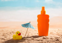 Sunscreen, umbrella and rubber duck in sand against sea.