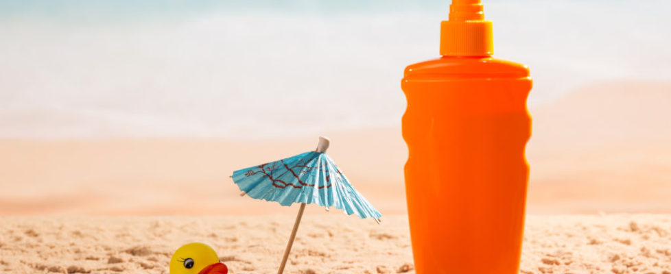 Sunscreen, umbrella and rubber duck in sand against sea.